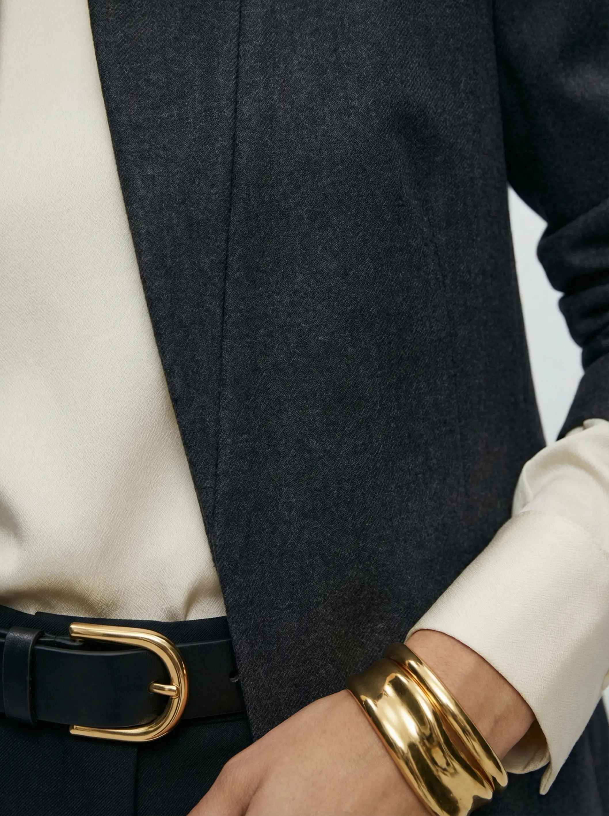 Macro detail of sculpted shoulder, wool texture and gold cuff with polished buckle.