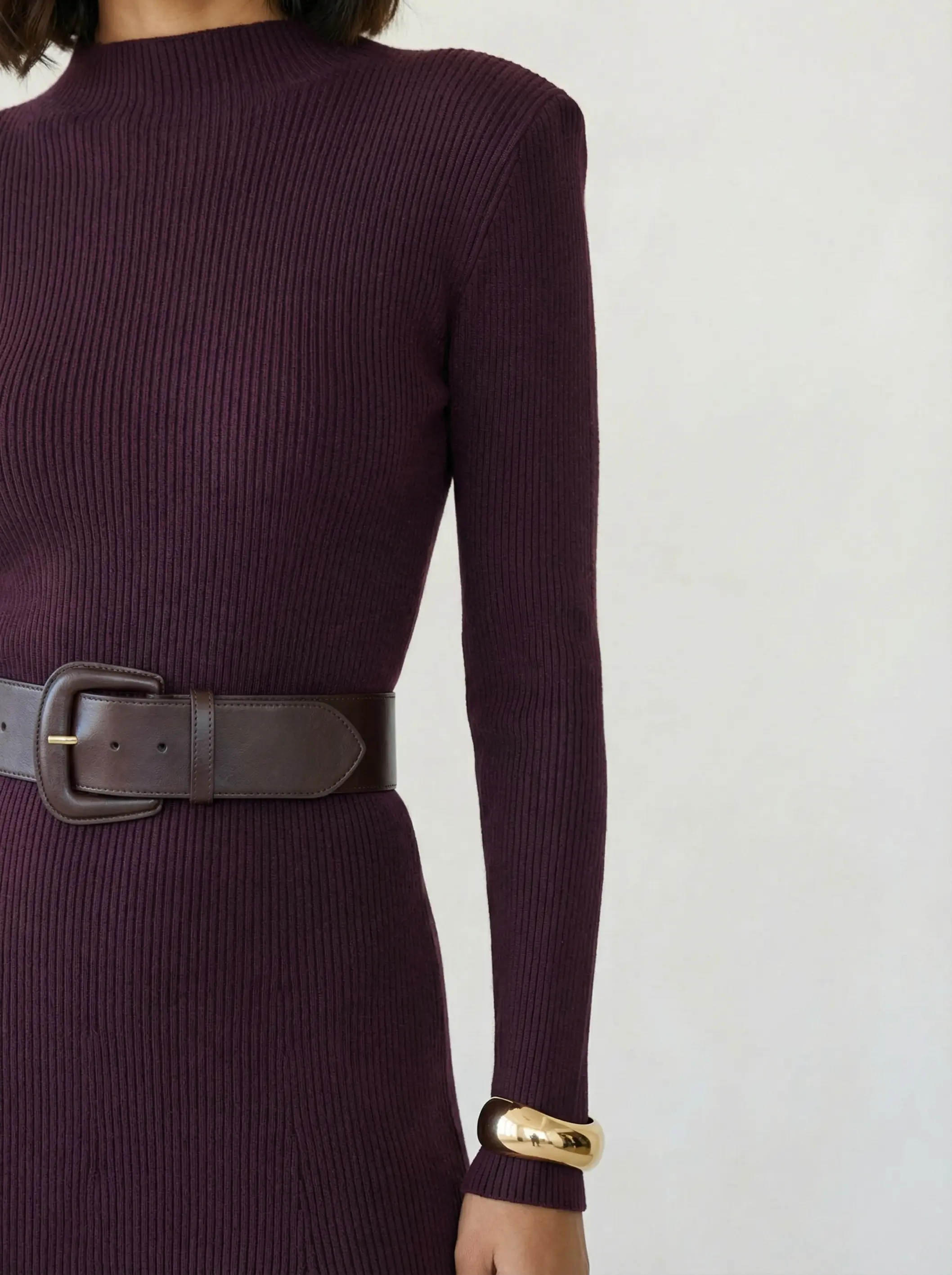 Close-up of leather belt buckle, knit shoulder texture and gold cuff detail.