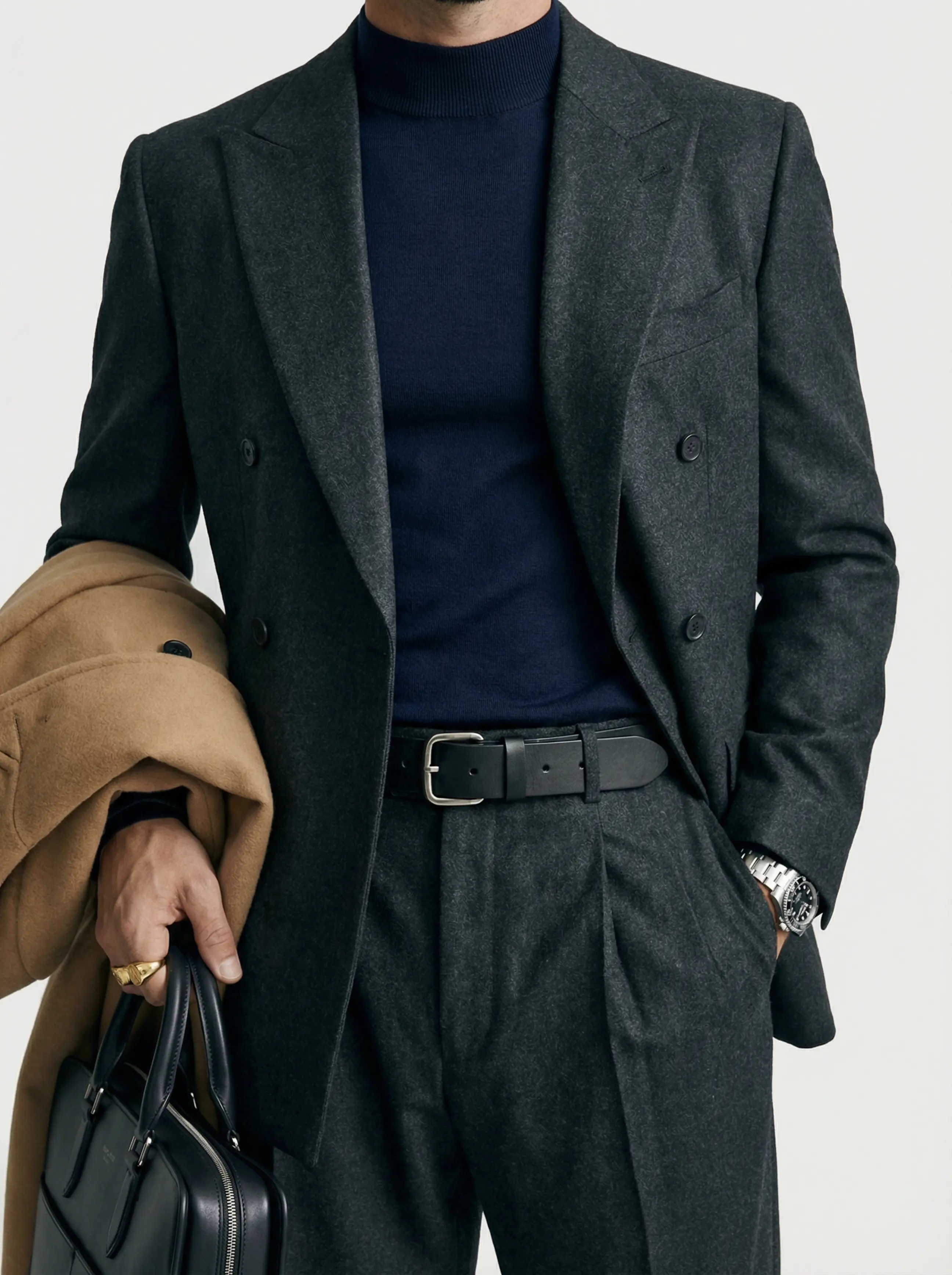 Macro detail of belt buckle threaded through trouser loops, wool lapel and gold signet ring.