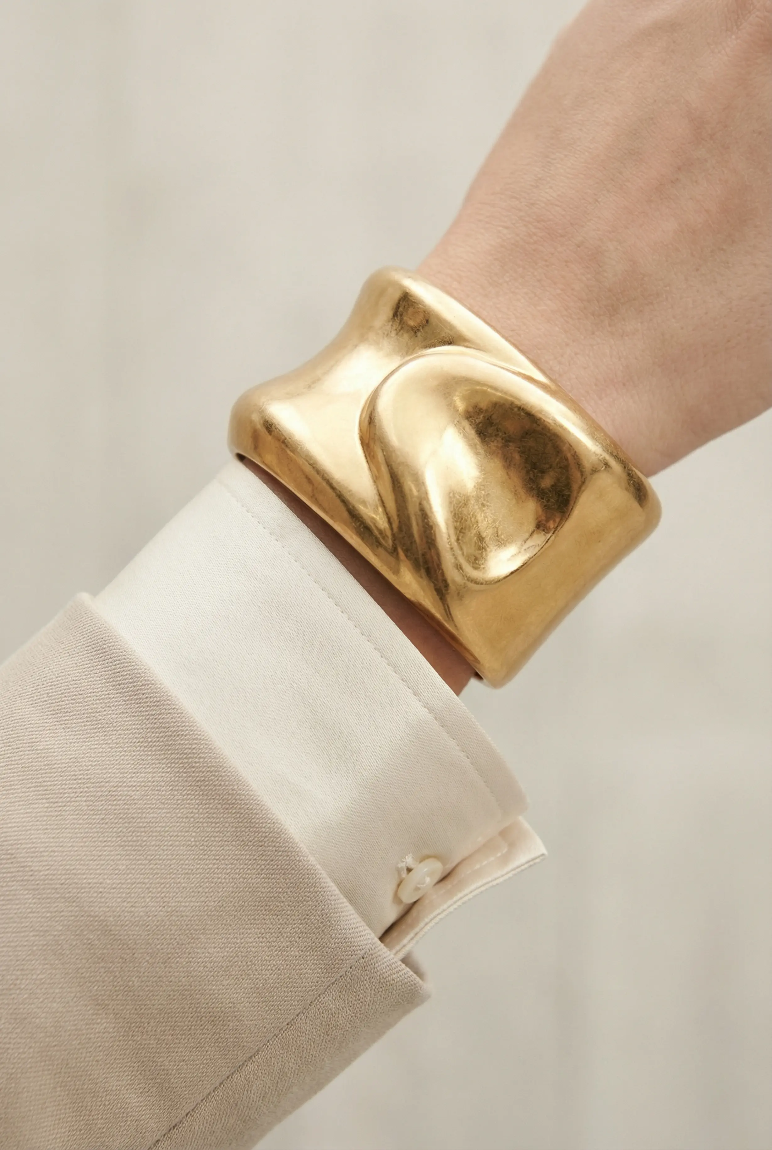 Macro detail of a bold gold cuff and silk high collar under a blazer sleeve