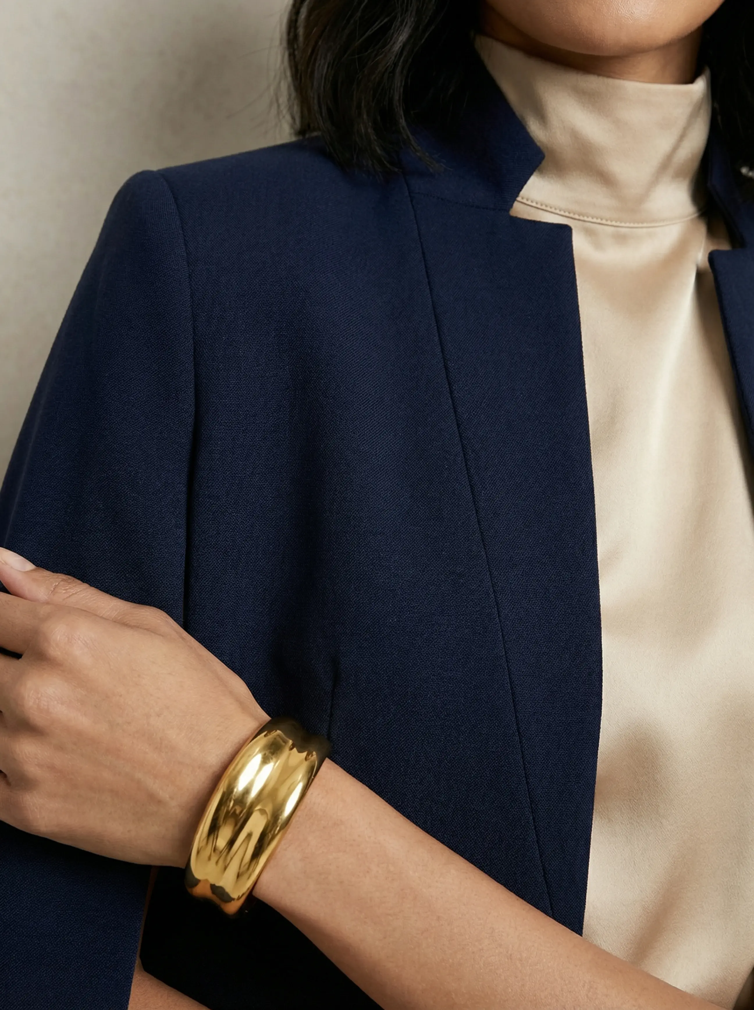 Macro detail of gold cuff, high-collar seam, and textured cape fabric.