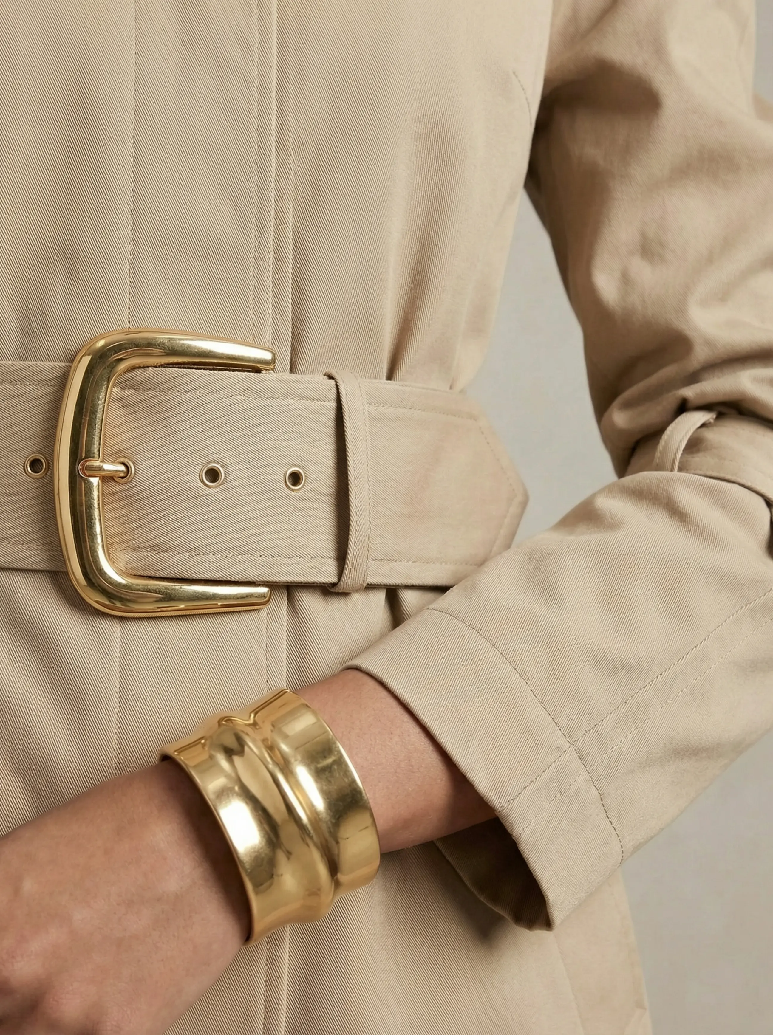 Close-up of statement belt buckle, textured fabric, and gold cuff bracelet on sleeve.