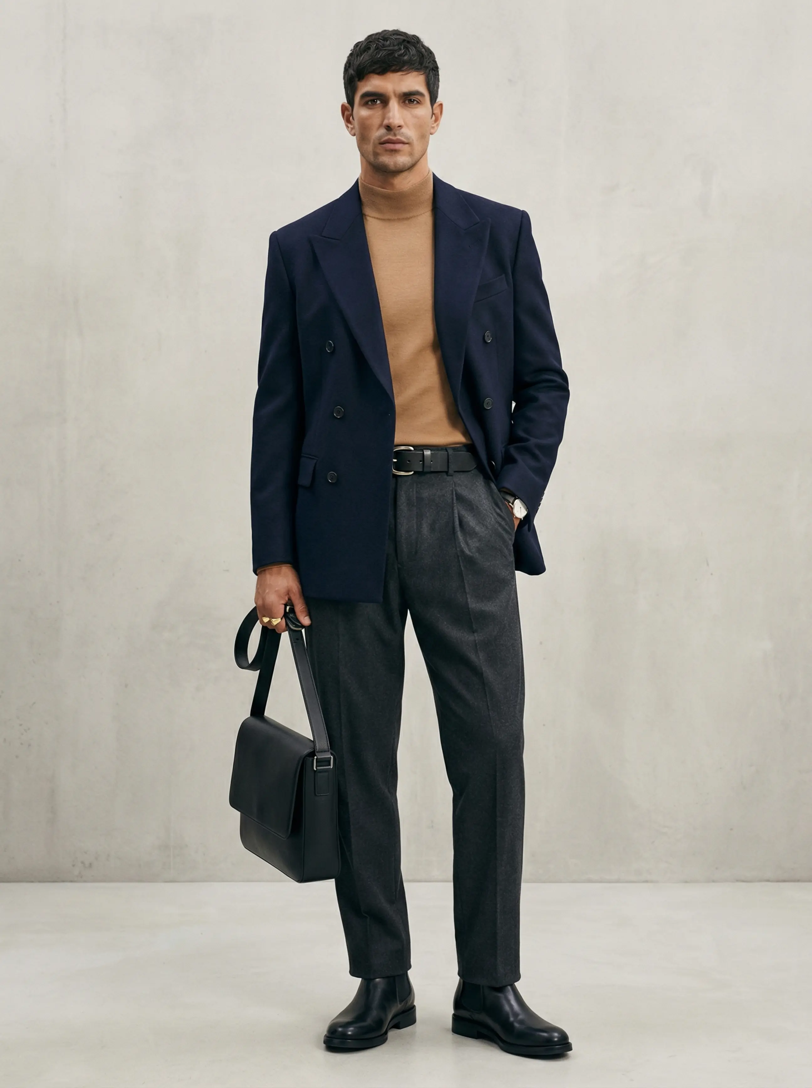 Full-body shot: man in sculpted double-breasted blazer, camel high-collar knit, charcoal trousers, chunky-buckle belt and Chelsea boots.