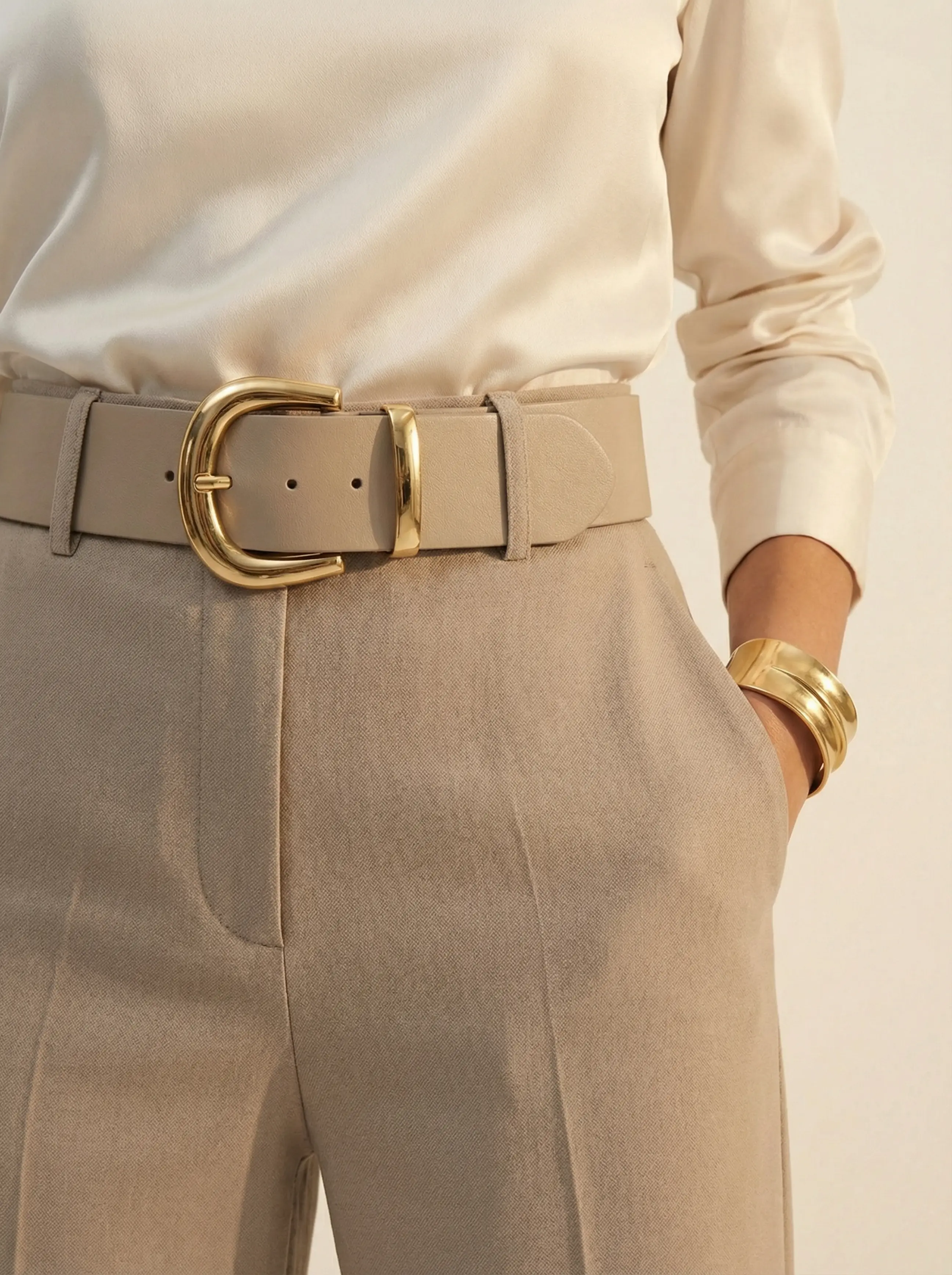 Close-up detail of chunky gold-buckled belt, wool texture and high-neck silk blouse