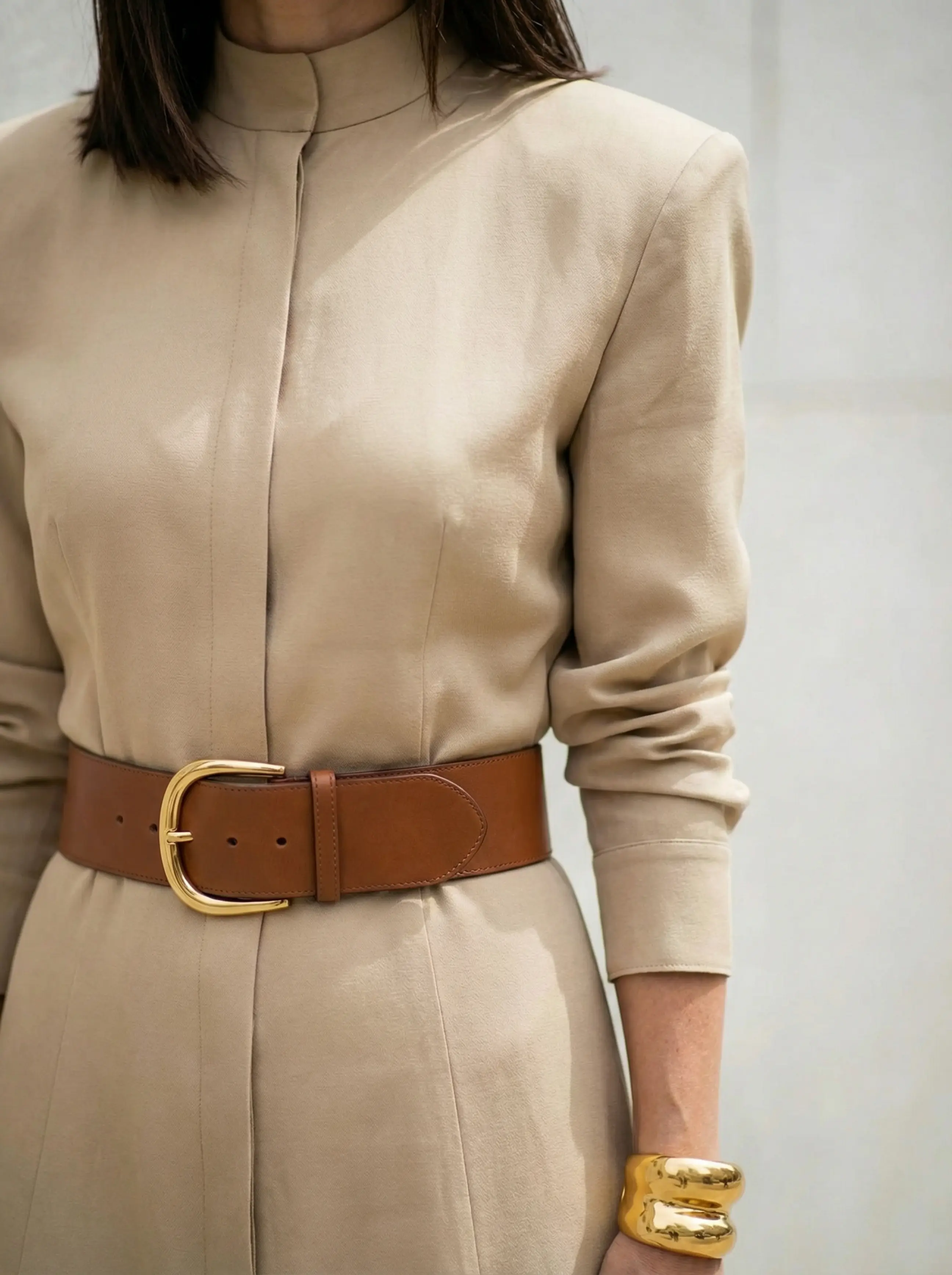 Close-up of chunky gold-buckled belt, silk texture, sculpted shoulder seam and gold cuff.