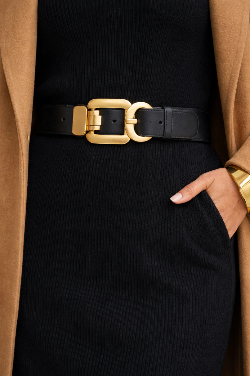 Macro close-up of brushed gold belt buckle on black ribbed knit dress with a gold cuff detail and camel coat edge.
