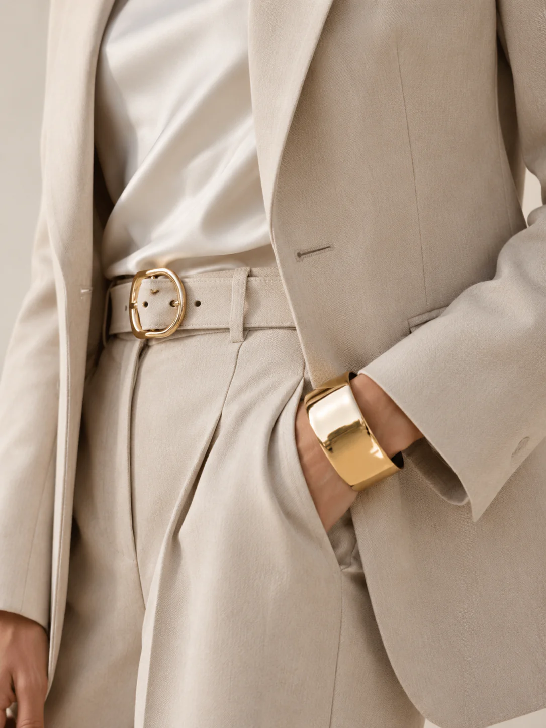 Macro shot of a gold cuff, belt buckle, and textured blazer fabric.