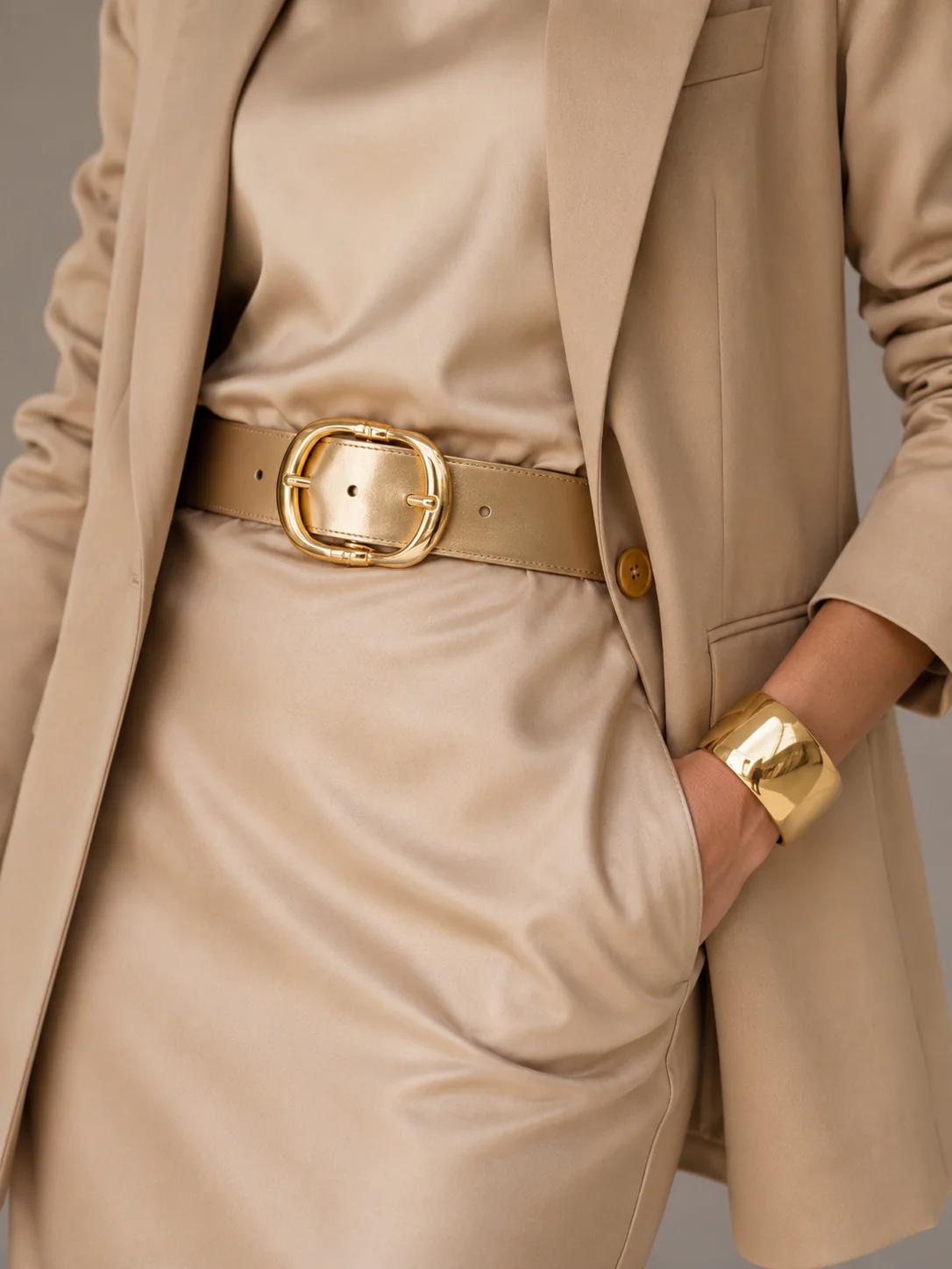 Macro detail of a gold belt buckle over champagne satin with polished texture.